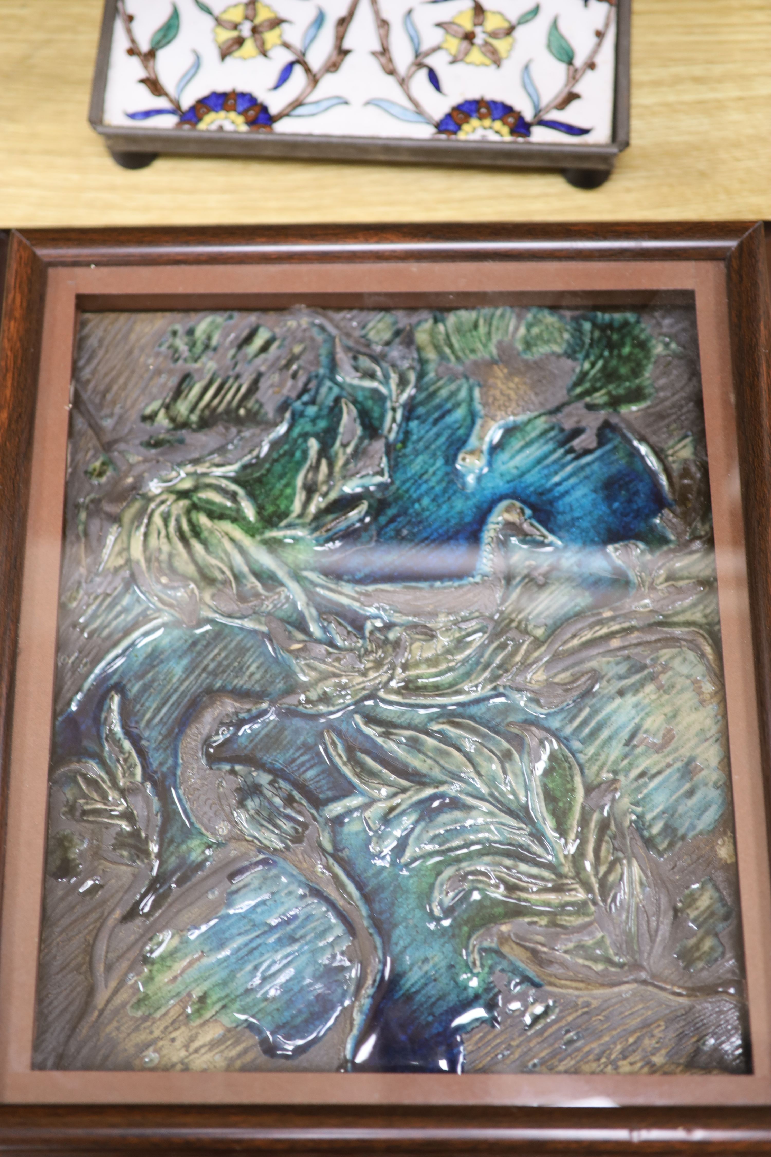 A framed glazed earthenware plaque, a tin glazed tile and one other